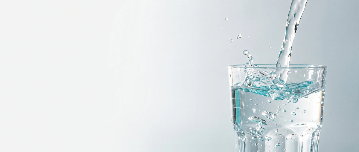 Eau pure versée dans un verre, éclaboussures cristallines sur fond clair — Filtrelia